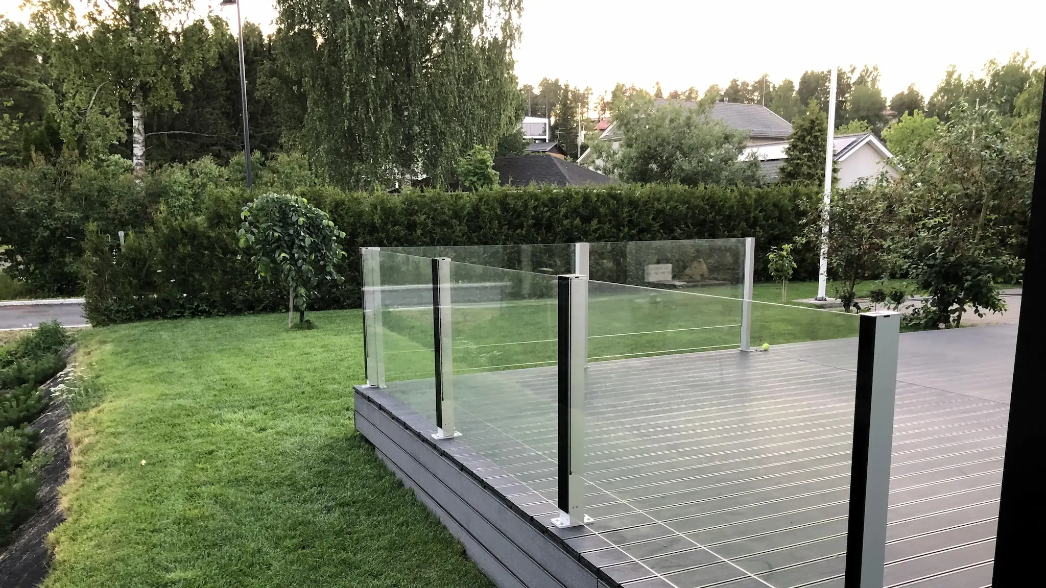Kiinteä lasikaide nurmikon reunassa – turvallinen ratkaisu pihan eri tasoille.