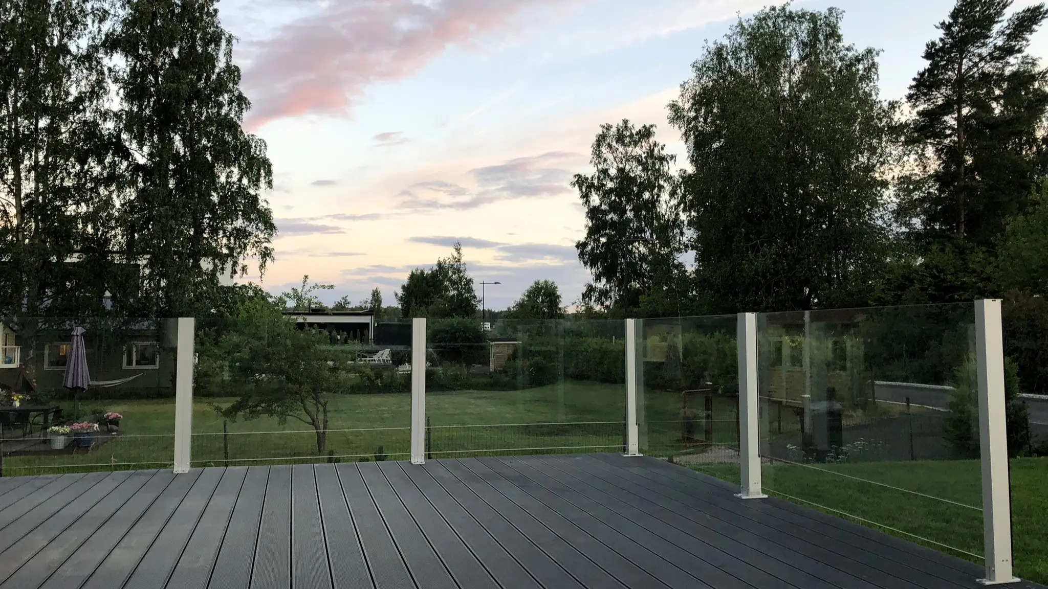 Kiinteä lasikaide avaralla nurmikkopihalla – valkoiset jalat ja huomaamaton näkymä.