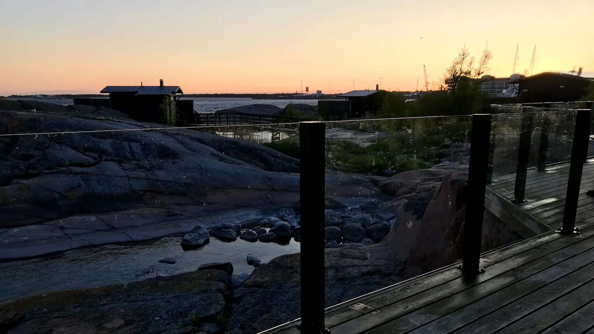 Auringonlasku kallioilla ja mustarunkoiset lasikaiteet Hangon saariravintolassa