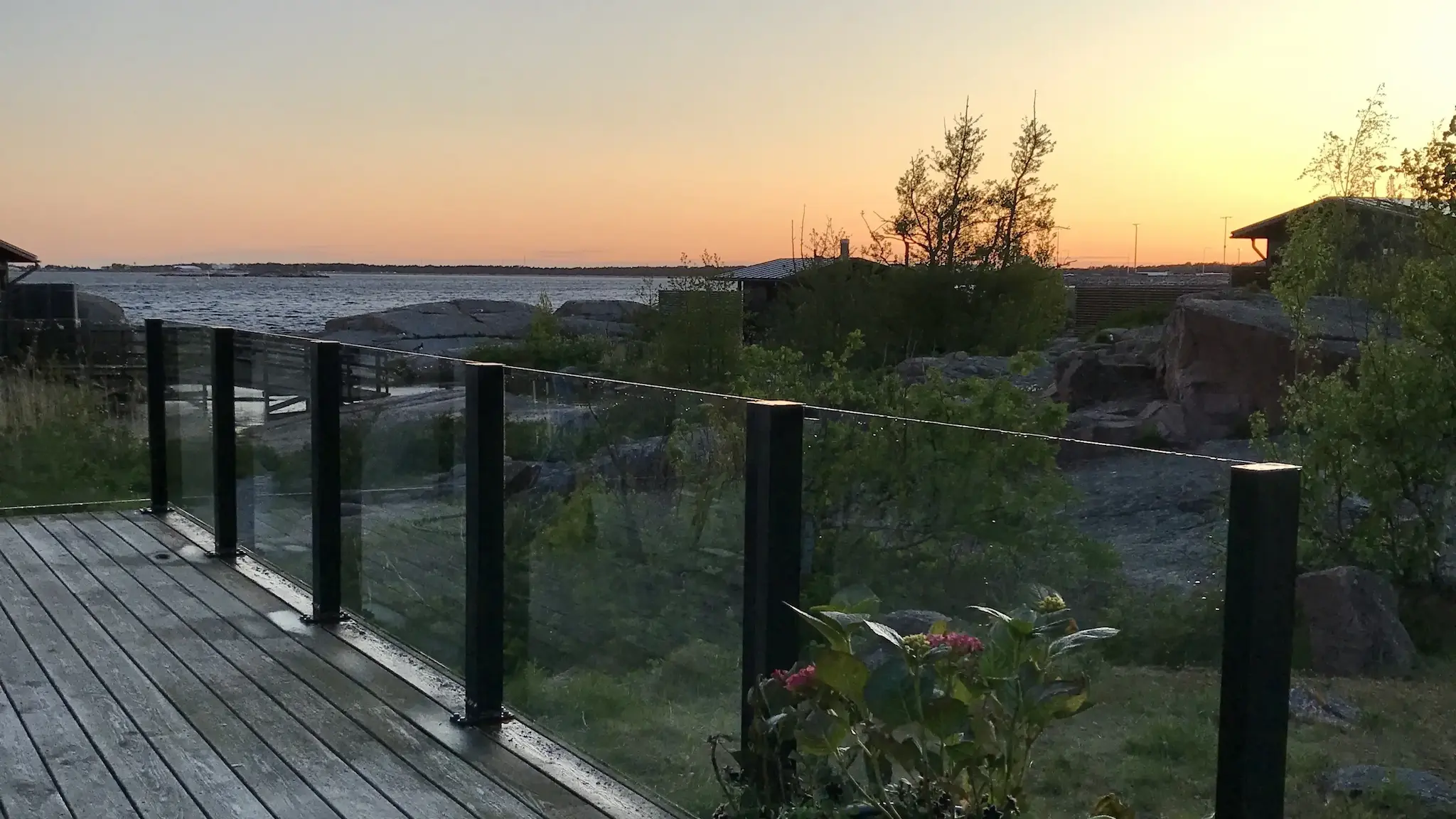 Kiinteä lasikaide saariravintolan kalliolla – musta runko ja auringonlaskun valo.