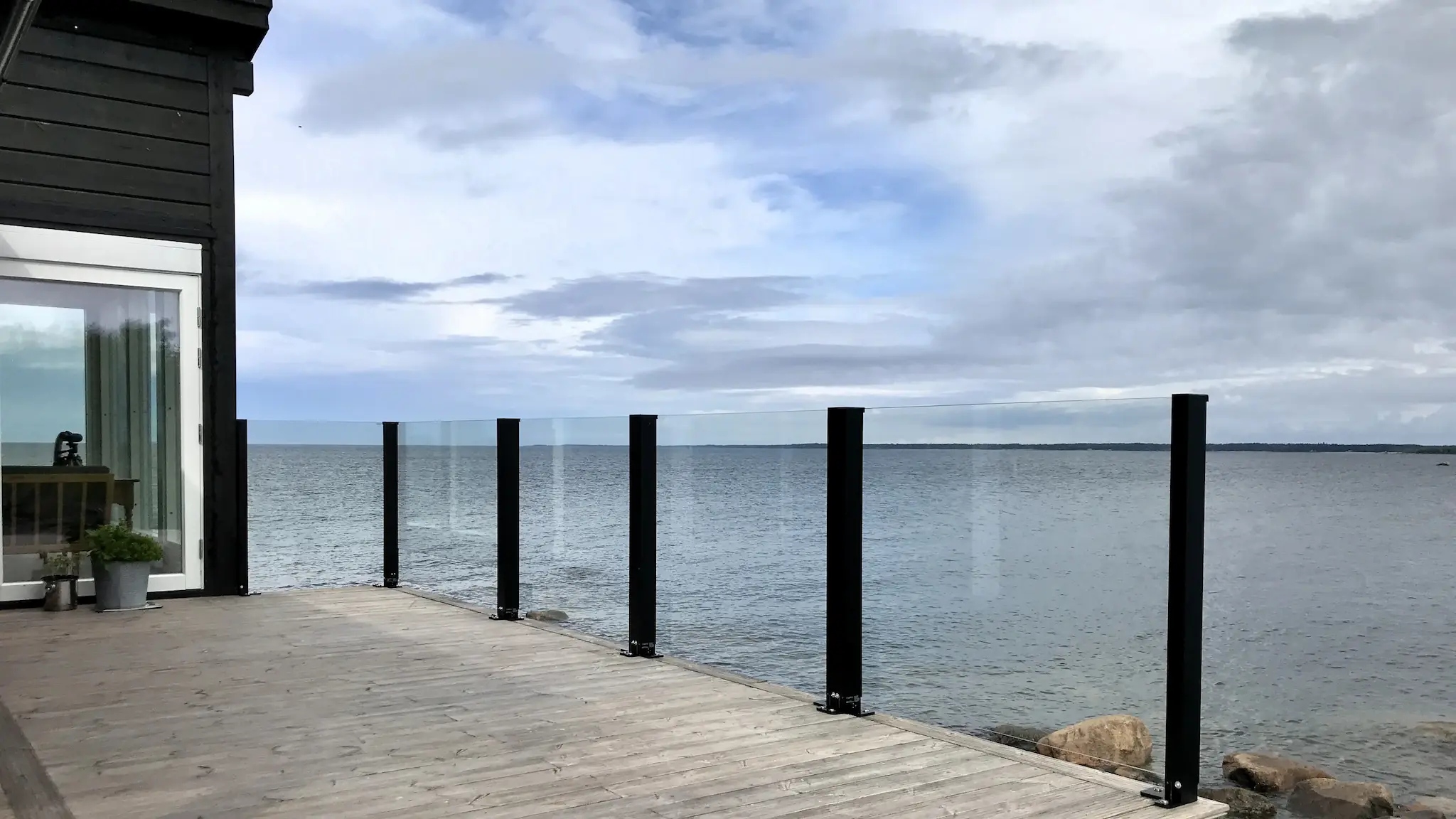 Kiinteä lasikaide rantaterassilla – avara maisema ja matala reunus.