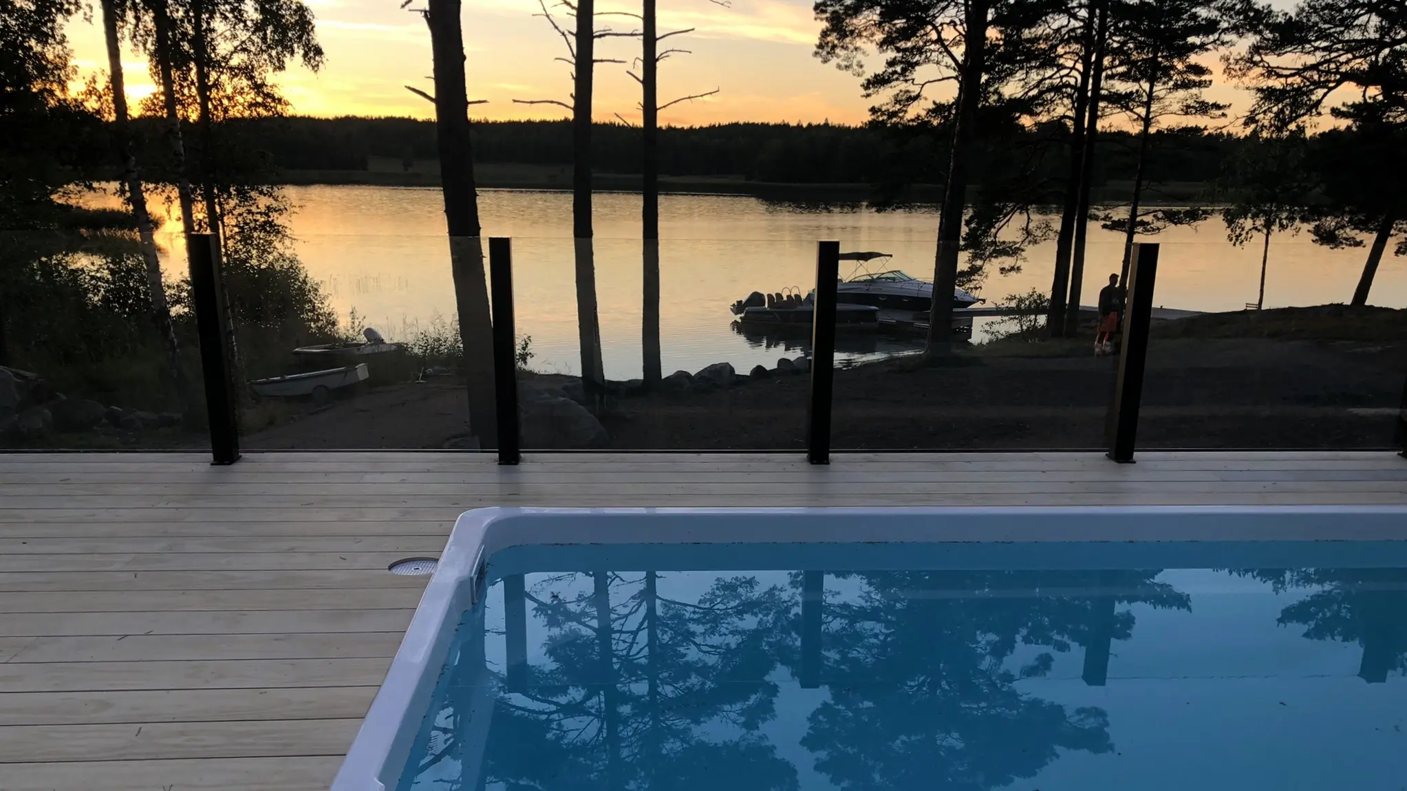 Kiinteä lasikaide terassilla ilta-auringossa – rauhallinen järvimaisema ja uima-allas.