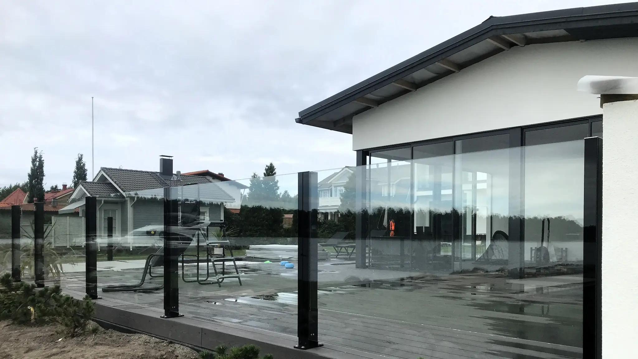 Kiinteä lasikaide modernin kivitalon edustalla – tummat jalat ja selkeä lasipinta.